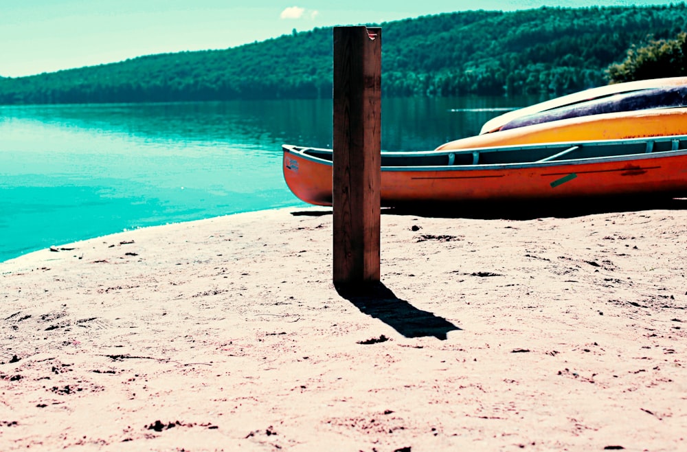 orange canoe on sand near body of water