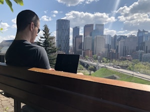 A traveler happily using a laptop to search for flights with a city skyline in the background.