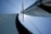 A close-up view of a sailboat's mast and sails against a clear blue sky. The sails are full and taut, capturing the wind, with one being predominantly white and the other black.
