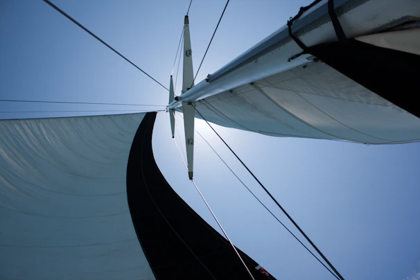 Close-up of a sailboat’s mast and sails catching the wind against a clear blue sky.