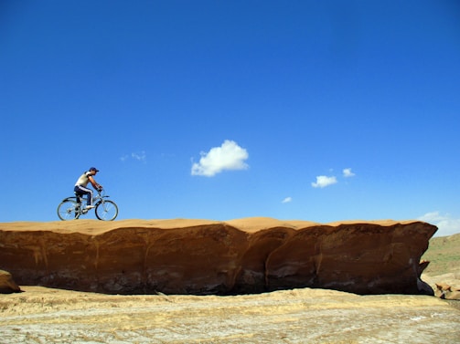 A scenic desert landscape with a cyclist riding along a dusty trail under a bright blue sky