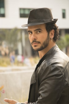 man in grey leather jacket and black hat looking over left shoulder
