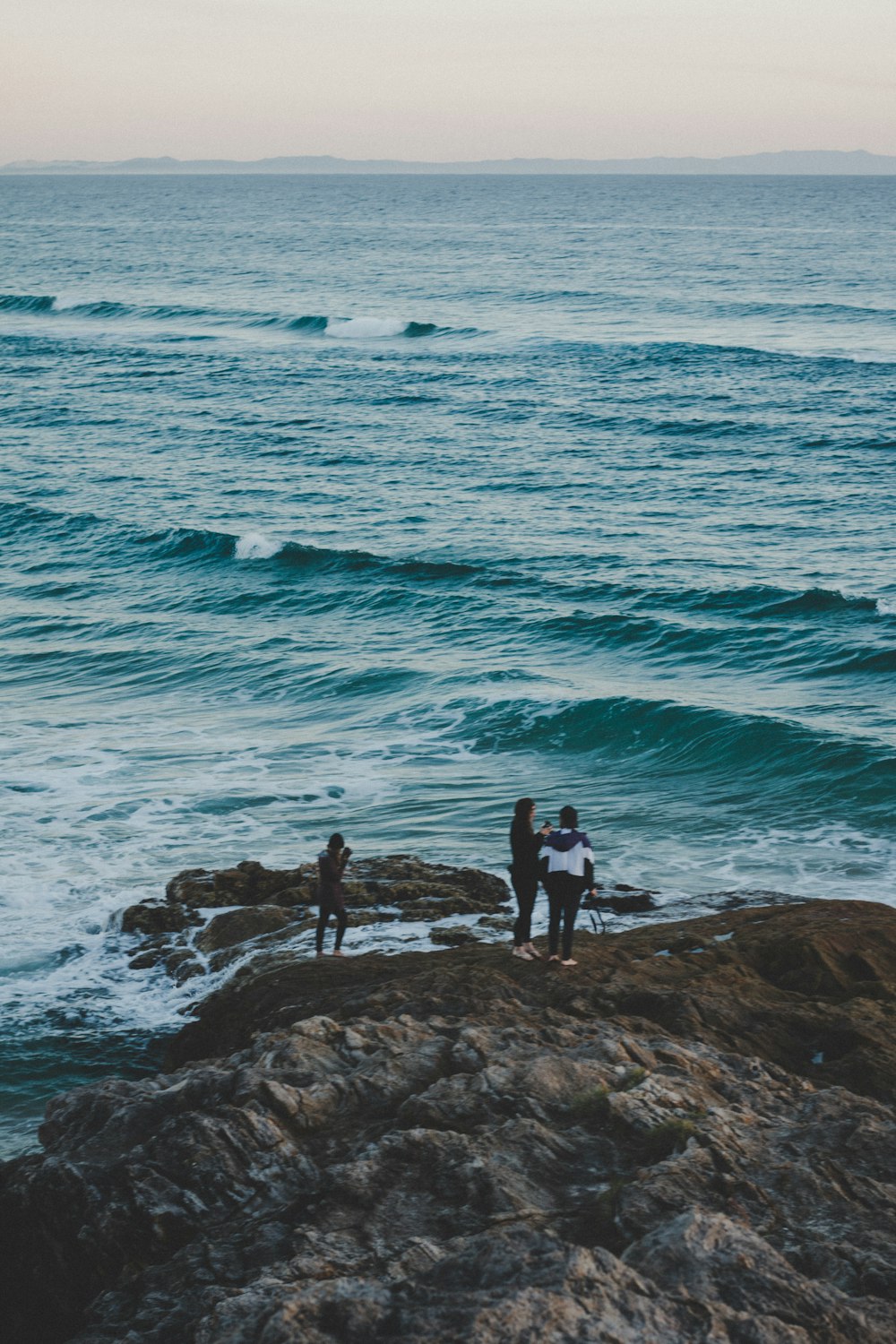 three people standing near beach cliff viewing blue calm sea
