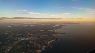 Aerial view of a private jet flying over a coastal landscape during sunset.