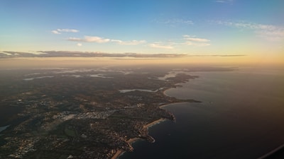 Aerial view of a private jet flying over a coastal landscape during sunset.