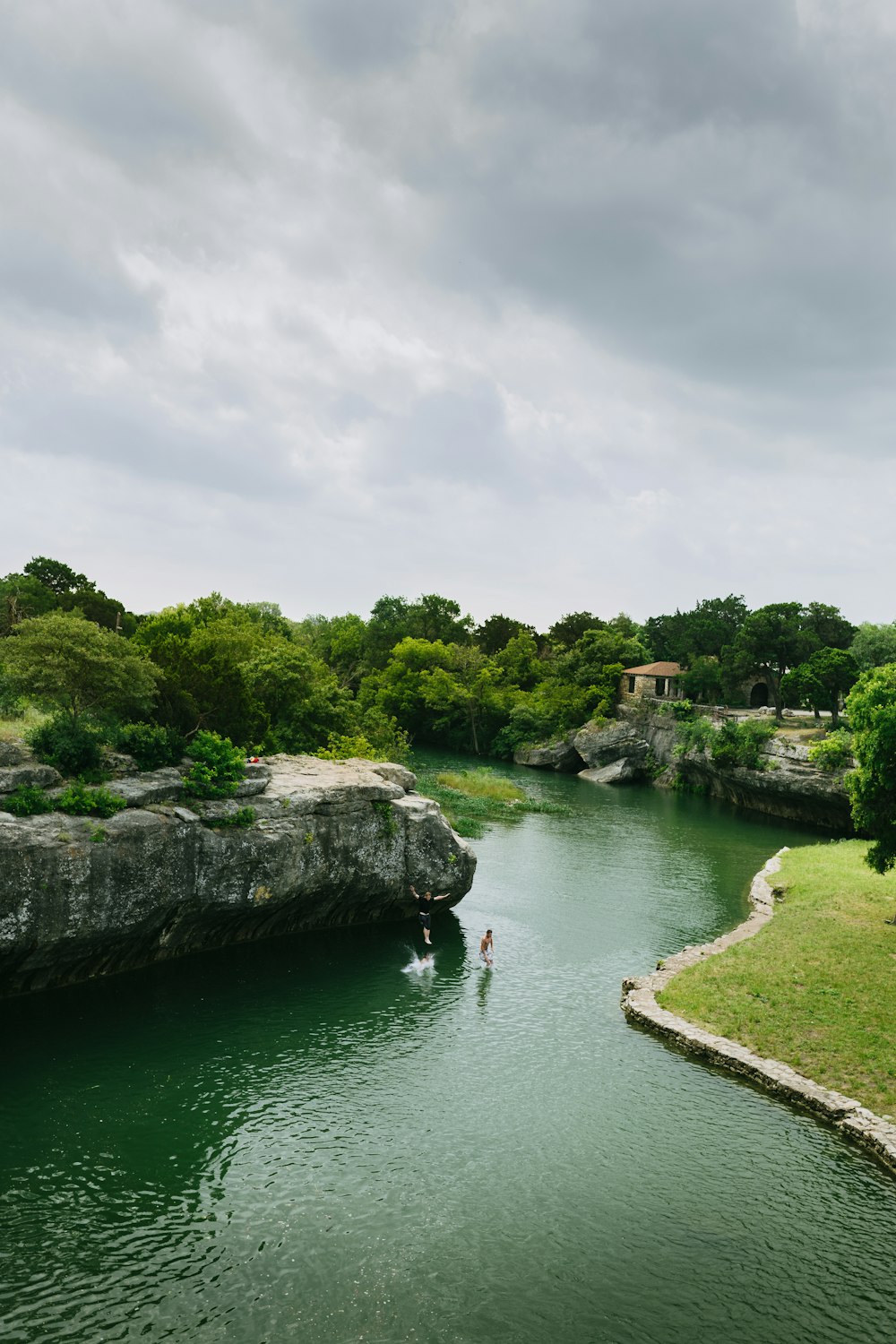 Persona en el lago que muestra el campo y los árboles altos bajo cielos blancos y grises