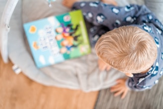 a little boy reading a book on a bed