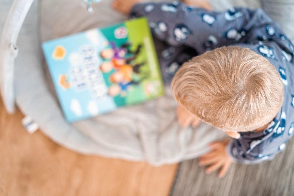 a little boy reading a book on a bed