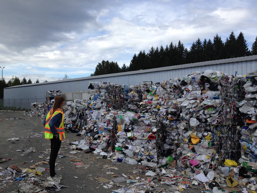 A person standing in front of stacked bins and sacks at a waste collection point.