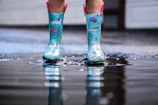 Stylish rubber boots splashed with water droplets on a rainy street.