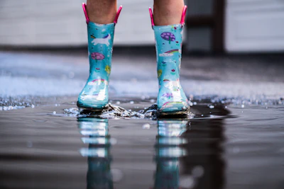 Stylish rubber boots splashed with water droplets on a rainy street.