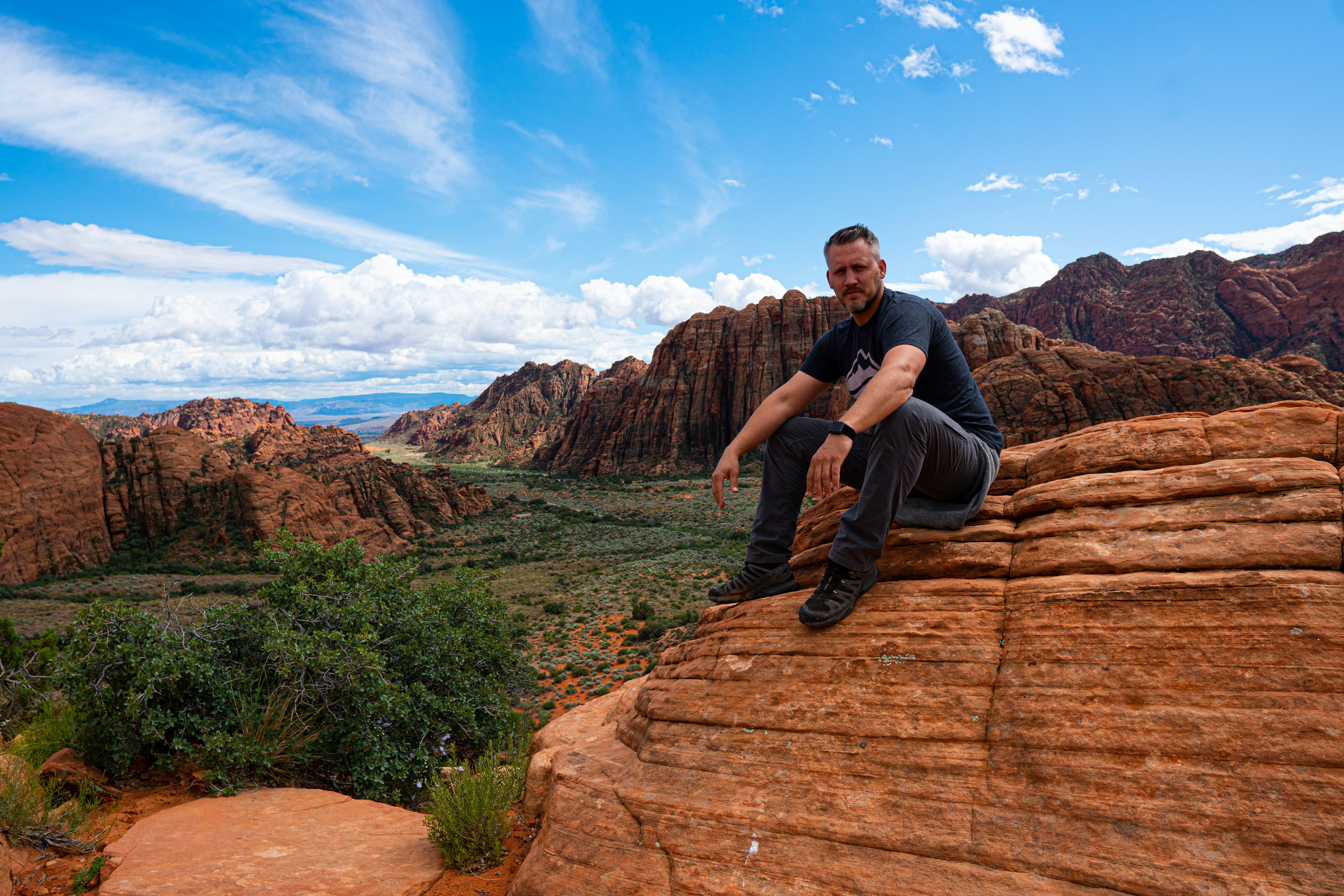 man wearing black shirt sitting on brown rock formation