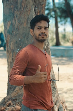 man standing near tree holding sunglasses