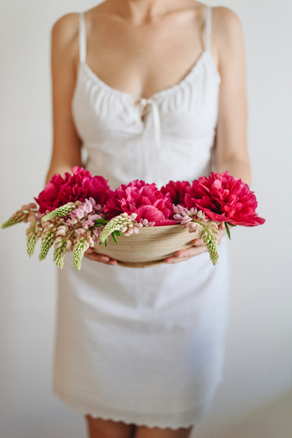 donna in vestito bianco che trasporta fiori rossi