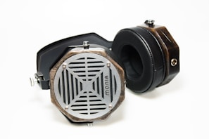 A pair of retro-style headphones with wooden casings, metal grills, and black padded ear cups lies on a white surface. The headphones feature hexagonal ear cups with a unique lattice design and a visible logo.