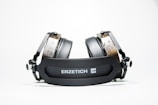 A pair of high-end headphones with black cushioned ear pads and wooden accents, resting on a flat surface. The headband prominently displays the brand name 'ERZETICH'. The design is modern and robust, with a focus on industrial aesthetics.