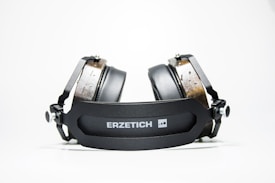 A pair of high-end headphones with black cushioned ear pads and wooden accents, resting on a flat surface. The headband prominently displays the brand name 'ERZETICH'. The design is modern and robust, with a focus on industrial aesthetics.