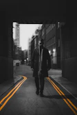 Model walking through a dimly lit alley wearing a flowing black coat with oversized typography on the back.