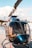 A sleek, glossy helicopter is parked on a wooden platform near a body of water, with calm skies and some clouds in the background. The helicopter's transparent windows reveal its interior seats, and its rotor blades are prominently visible.