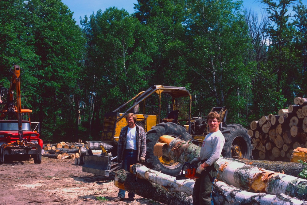 two men standing near cut logs beside trees