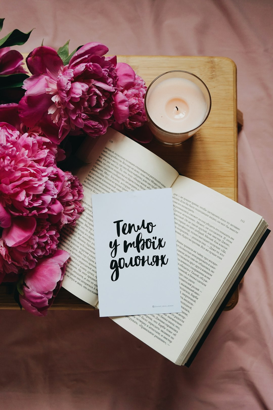 white and black labeled book beside white candle jar on top of brown wooden table