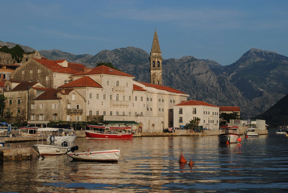 White and red boats moored along the Perast waterfront near stone buildings