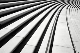A series of parallel, curved concrete steps with strong shadows creating a geometric pattern. The steps appear to form a modern architectural element, sweeping in an elegant curve that adds a dynamic visual flow.