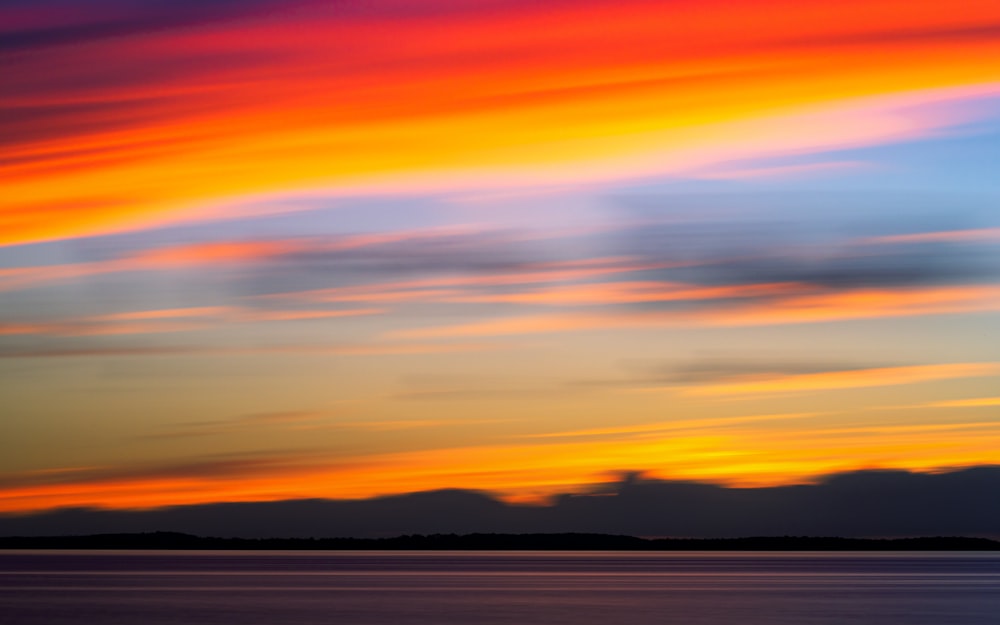 a plane flying over a body of water under a colorful sky