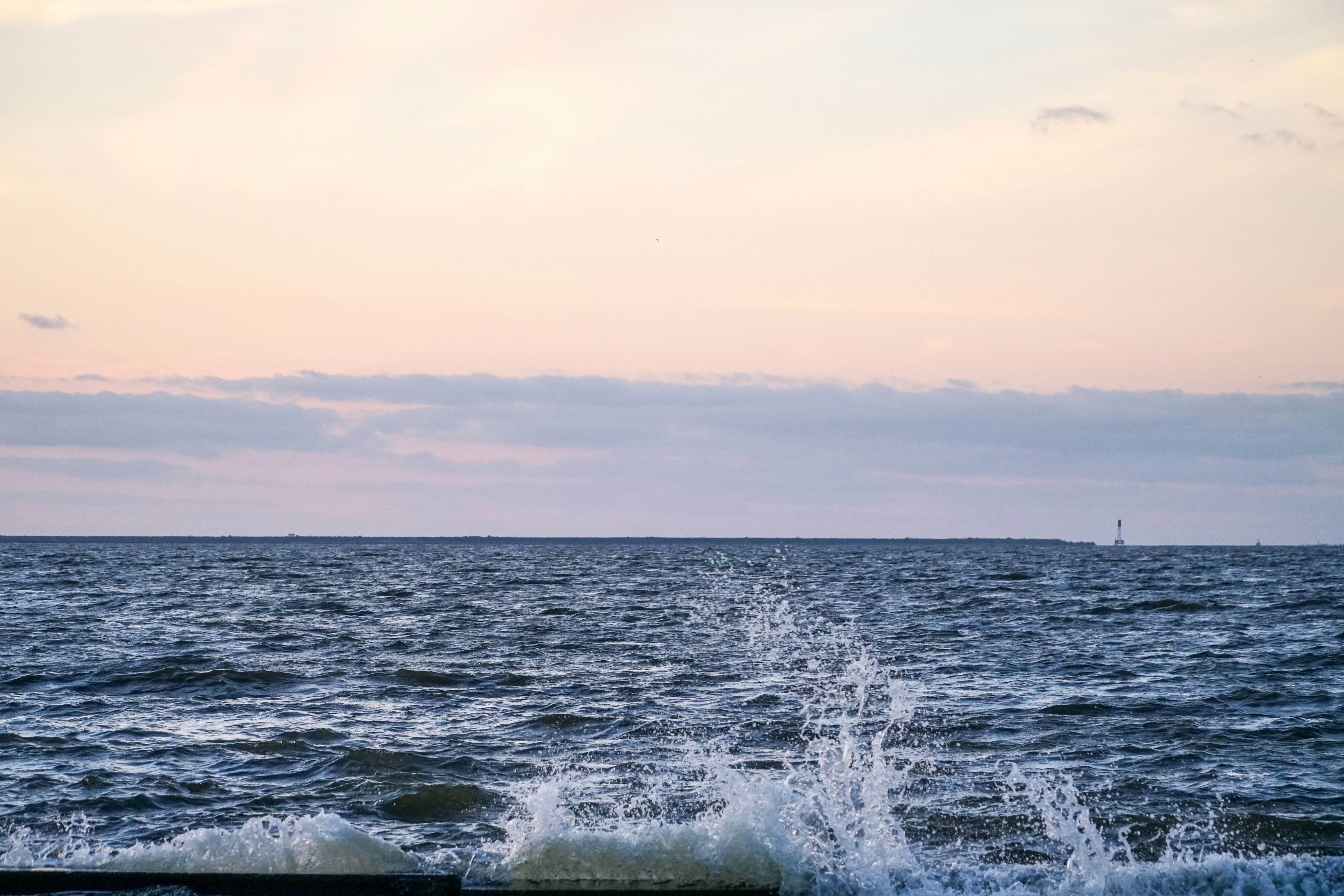 sea waves during daytime, Ocean water spray crashing against a coastal barrier wall creating splashing waves early in the morning with a pastel sky.