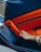 A hand with painted nails reaches for the bright orange interior panel of a car door, featuring contrasting blue elements and visible speaker and stitch details.