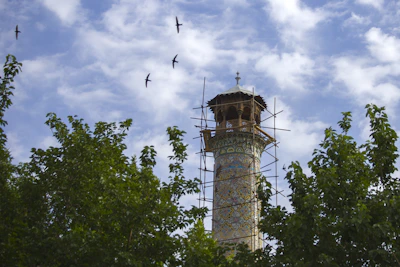 A skilled climber painting a tall mosque minaret with precision and care.