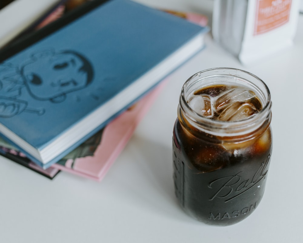 Einmachglas aus klarem Glas mit Cola und Eiswürfeln auf dem Tisch neben Notizbüchern