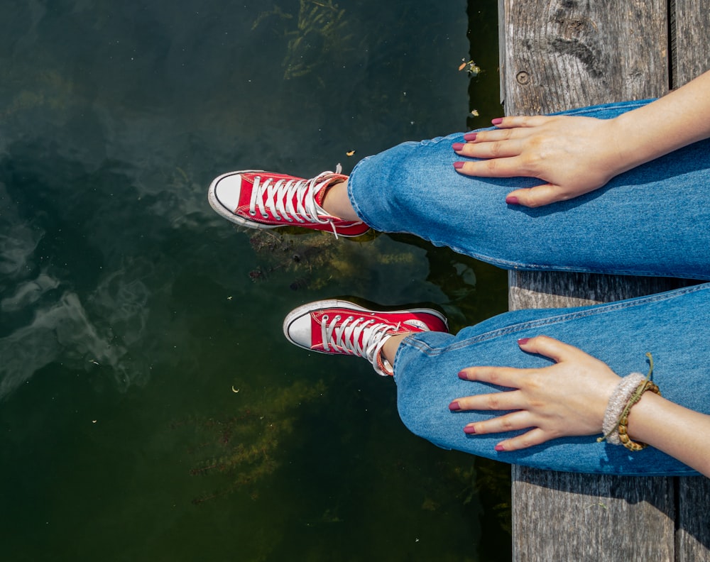 person wearing denim jeans sitting on wooden dock during daytime