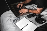 A young woman typing on a laptop with notes and a book about intellectual property beside her.