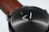 A close-up of a sleek wristwatch with a dark, metallic face and minimalistic hour markers. The watch has a simple, elegant design with a brown leather strap attached to a polished metal case.