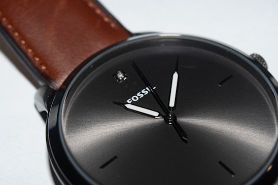 A close-up of a sleek, minimalist wristwatch resting on a wooden table beside a leather-bound notebook.