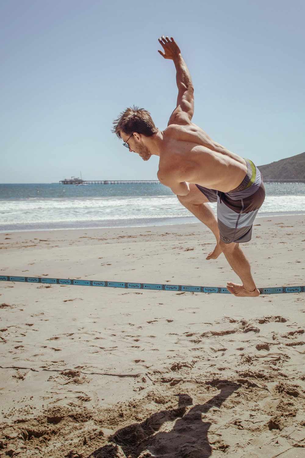 uomo in occhiali da sole e pantaloncini da surf che cammina sulla corda