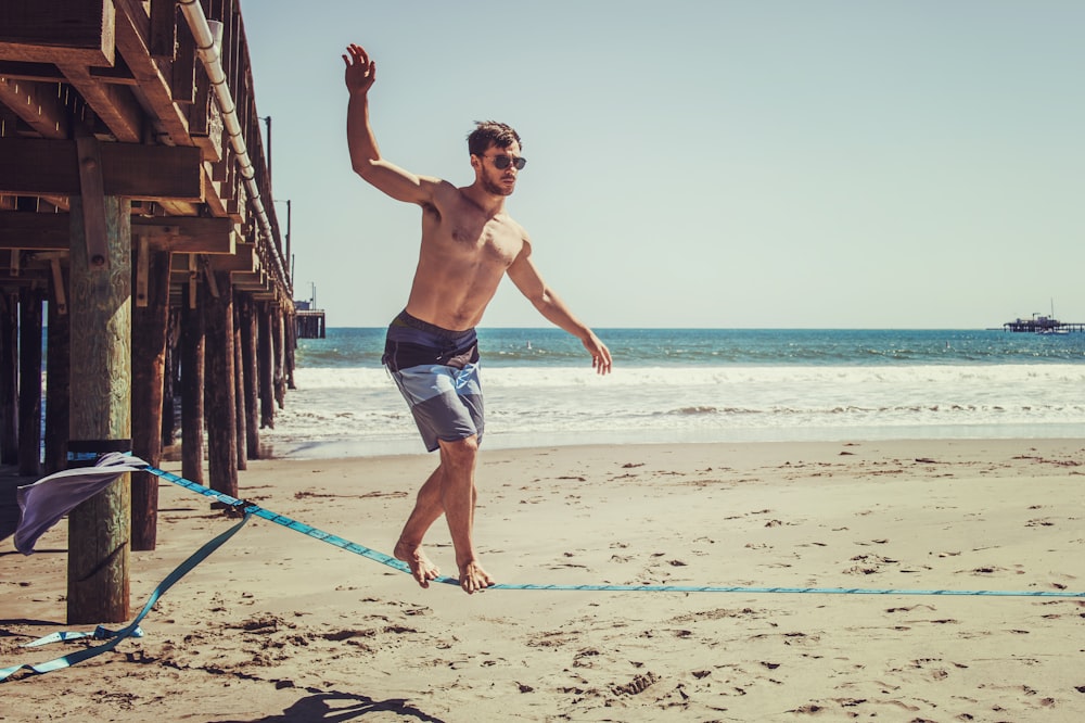 man wearing sunglasses and board shorts standing on rope