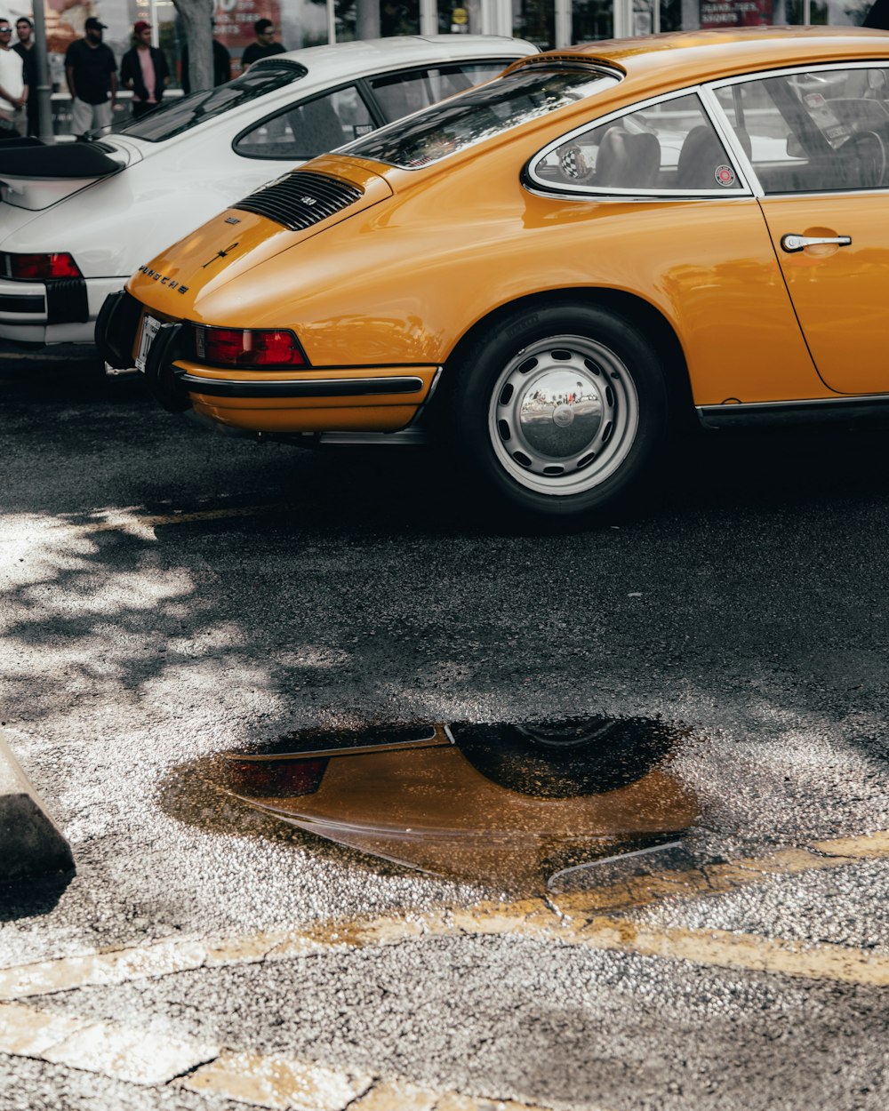 Classica coupé arancione vicino a una pozzanghera d'acqua sulla strada durante il giorno