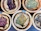 Several wicker baskets filled with various dried herbs and flowers, each with a small wooden sign labeling the contents. The herbs are displayed on a dark surface, and the baskets have a rustic appeal.