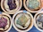 Several wicker baskets filled with various dried herbs and flowers, each with a small wooden sign labeling the contents. The herbs are displayed on a dark surface, and the baskets have a rustic appeal.