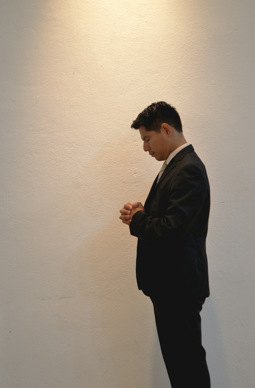 man prays in front white painted wall