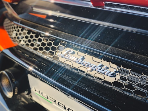 A close-up of a car featuring a honeycomb-patterned grille and the metallic logo of a luxury car brand prominently displayed. The image captures the play of light across the shiny surface, highlighting the premium finish and design elements.