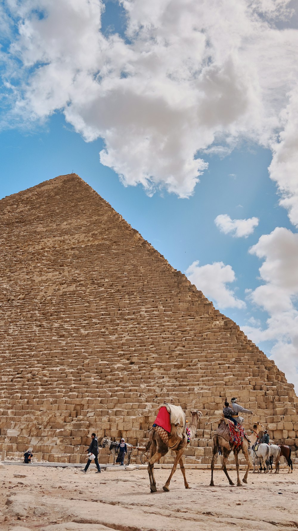 people riding camels by pyramid during daytime