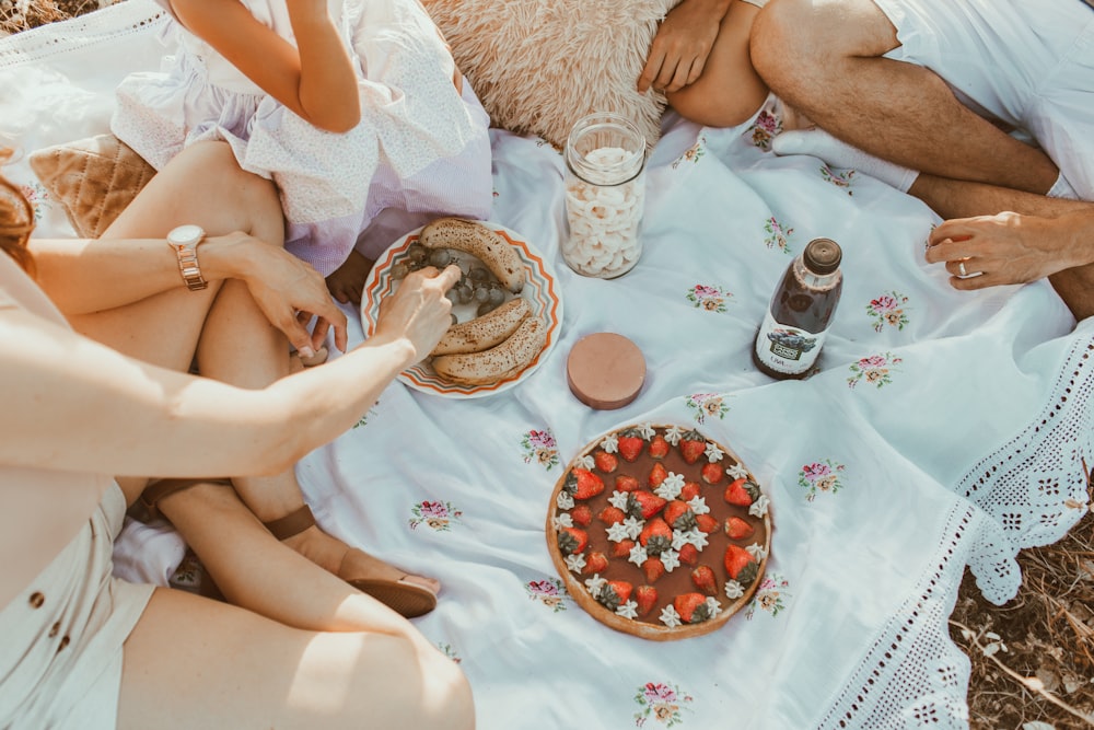 pessoas sentadas em tecido branco comendo pão perto do bolo