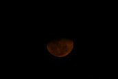 A partially visible reddish moon is set against a dark sky, suggesting a lunar eclipse or an appearance during sunset.