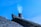 A rooftop with traditional dark tiles and a brick chimney emitting a faint trail of smoke against a clear blue sky.