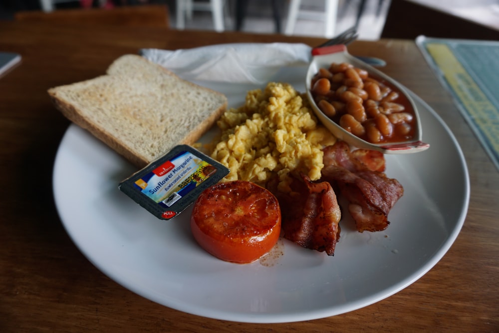 plate of breakfast meal with beans, scrambled egg, bacon and slice of bread