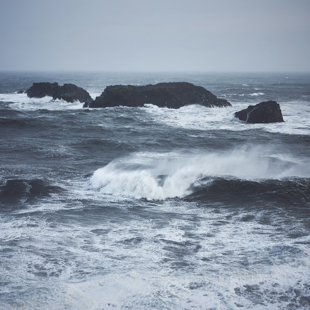 crashing waves and rocky islands during day