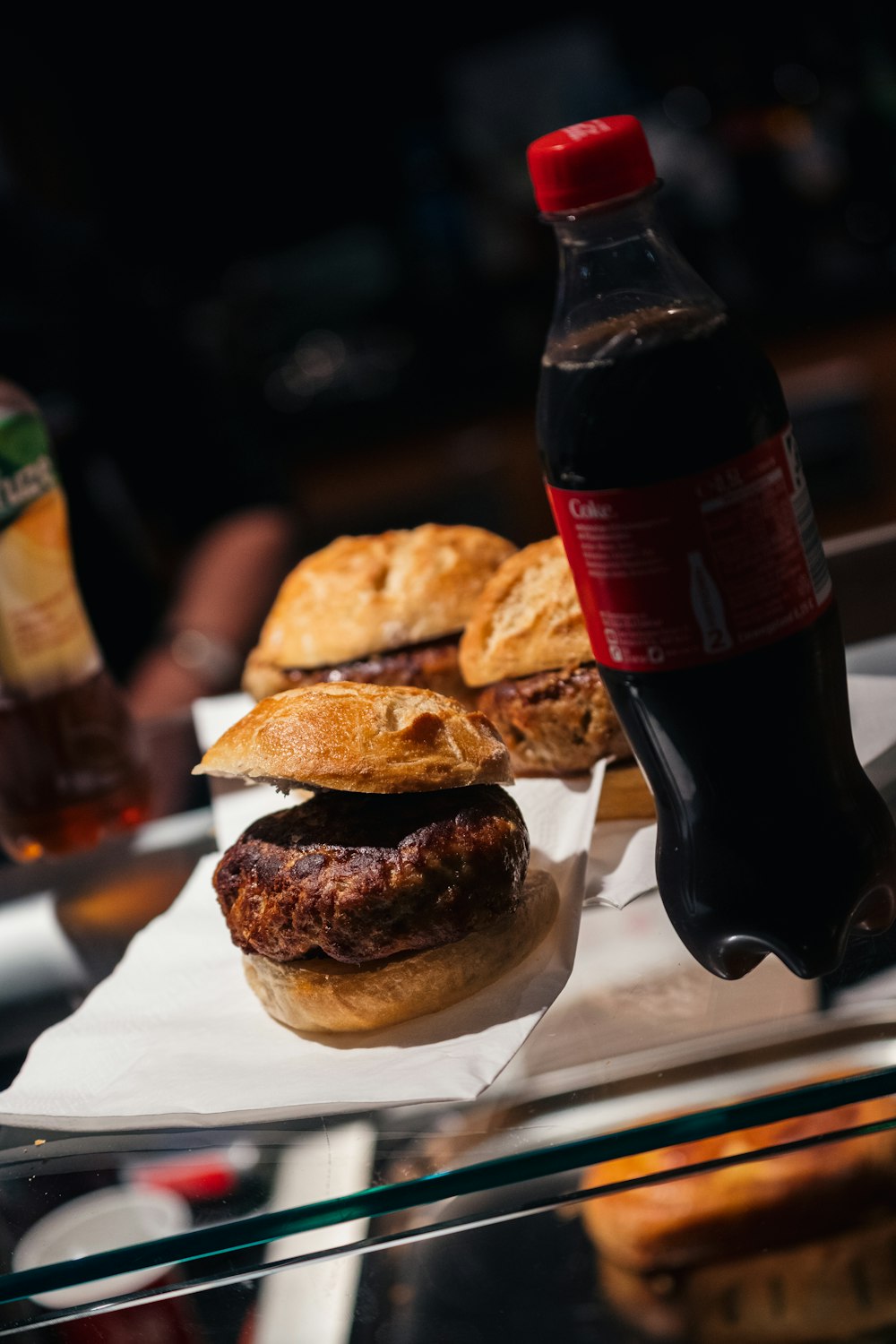 three burgers and bottle of Coca-Cola on table